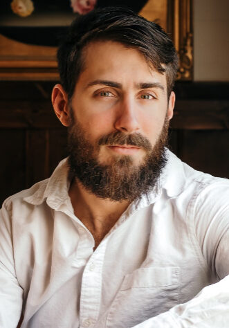Jaymes A man with beard and mustache sitting in front of a painting.